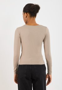 Maglia a maniche lunghe, aderente, in beige chiaro, realizzata in tessuto a costine. Collo rotondo, spalle senza cuciture, abbinata a jeans scuri a vita alta.