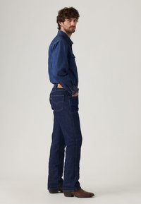 Chaqueta de denim y jeans en azul oscuro, con bolsillos clásicos, diseño de pierna recta y costuras en contraste. Botas marrones completan el atuendo.
