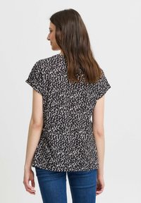 T-shirt noir à manches courtes avec un motif abstrait blanc, en tissu doux, coupe ample, ourlet arrondi et texture subtile, associé à un jean en denim bleu.