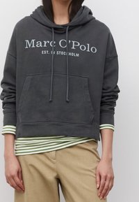 Donkergrijze katoenen hoodie met een voorzak, trekkoorden en bedrukte tekst. Gedragen over een groen-wit gestreept shirt met een ronde hals.