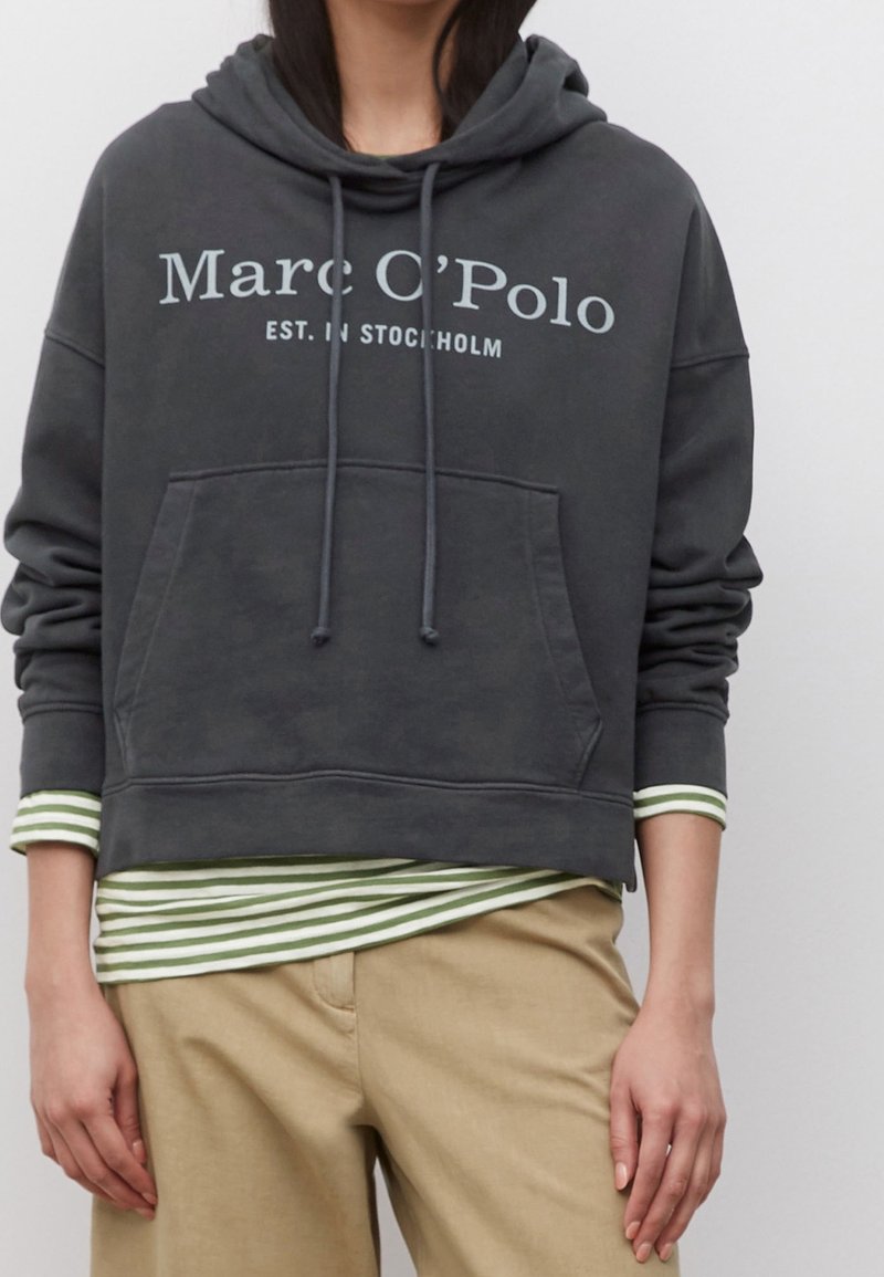 Donkergrijze katoenen hoodie met een voorzak, trekkoorden en bedrukte tekst. Gedragen over een groen-wit gestreept shirt met een ronde hals.