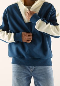 Pullover color-blocked blu e crema con zip a quarto di giro, polsini e vita a coste. Realizzato in tessuto morbido con una vestibilità comoda.