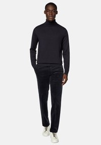 Navy turtleneck sweater, paired with dark corduroy pants. Model wears white sneakers with gray laces. Simple, streamlined design.