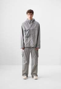 Light grey jacket and cargo pants made of a textured, lightweight fabric. Jacket features a front pocket, adjustable hood, and loose fit.