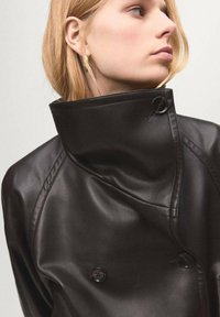 Czarna skórzana kurtka z wysokim kołnierzem, podwójnym zapięciem, wyraźnym przeszyciem i błyszczącymi guzikami. Gładkie, teksturowane wykończenie.