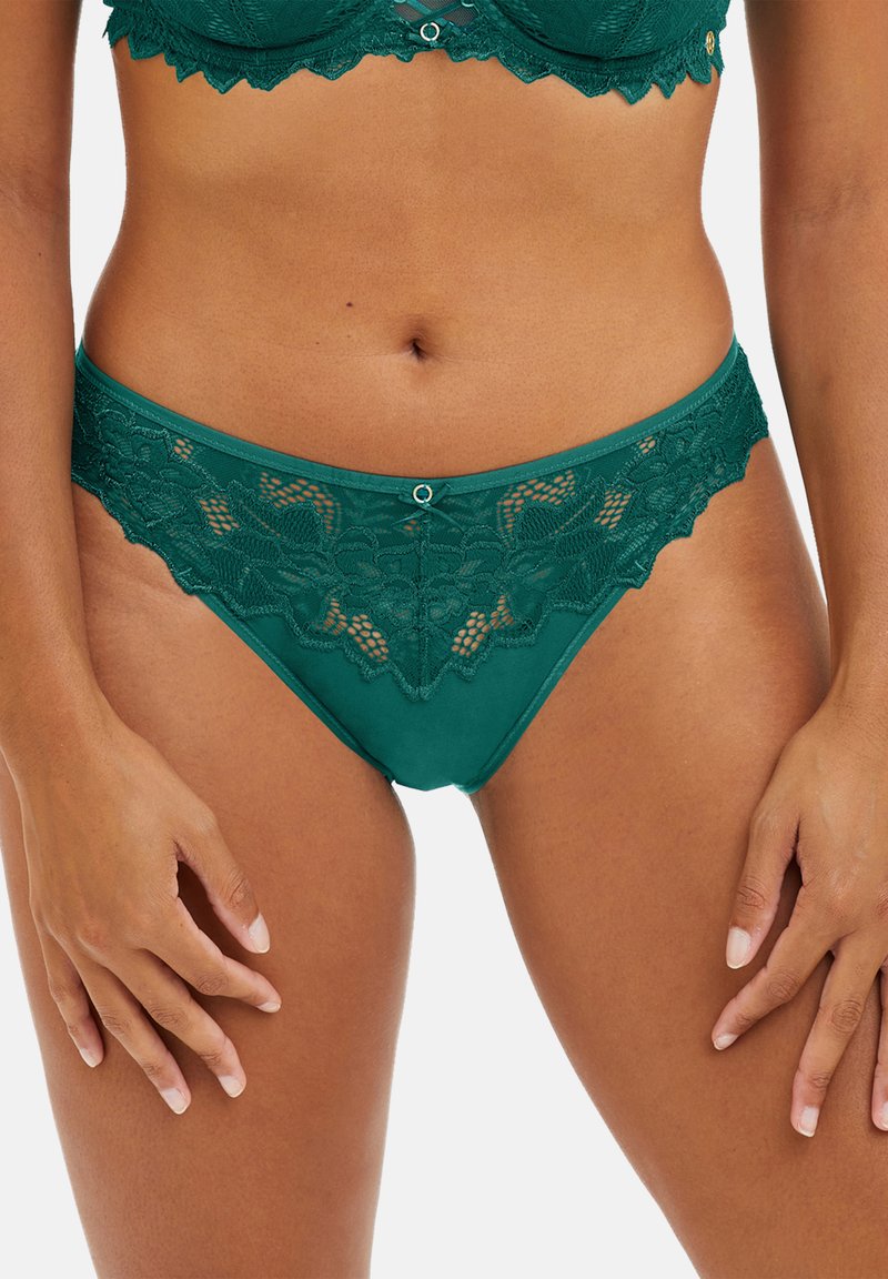 String en dentelle vert émeraude avec motifs floraux, présentant une taille lisse et de délicats bords festonnés. Accent avec un anneau décoratif à l'avant.