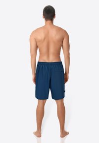 Marineblaue Badehose aus leichtem Stoff, mit elastischem Bund, seitlichen Taschen und einer Gesäßtasche. Schmeichelnde Textur.