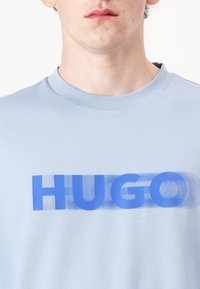 Light blue cotton t-shirt featuring a bold, blue "HUGO" graphic across the chest. Short sleeves and a round neckline.