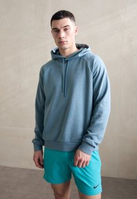 Svetlomodrá mikina s kapucňou a dlhým rukávom, s raglanovými rukávmi a predným vreckom, spojená s tyrkysovými šortkami s malým logom.