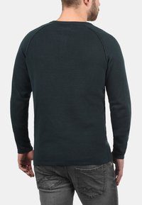 Donkergroen pullovertrui met ribbelstructuur, lange mouwen en een ronde halslijn, aangevuld met een reguliere pasvorm en een eenvoudig ontwerp.
