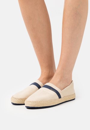 Beige Canvas-Slipper mit navyblauen Akzenten und gewebten Espadrille-Sohlen, ausgestattet mit einer runden Zehenpartie und dezentem Branding im Obermaterial.