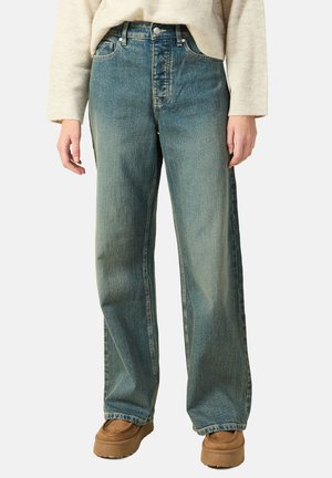 Breda blå jeans i denim med en blekt tvätt, fem fickor och en knappstängning. Bärs med bruna skor.