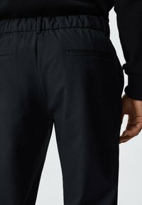 Černé kalhoty s elastickým pasem, vybavené dvěma zadními kapsami a hladkou, lehkou tkaninou. Střih na míru s moderním designem.