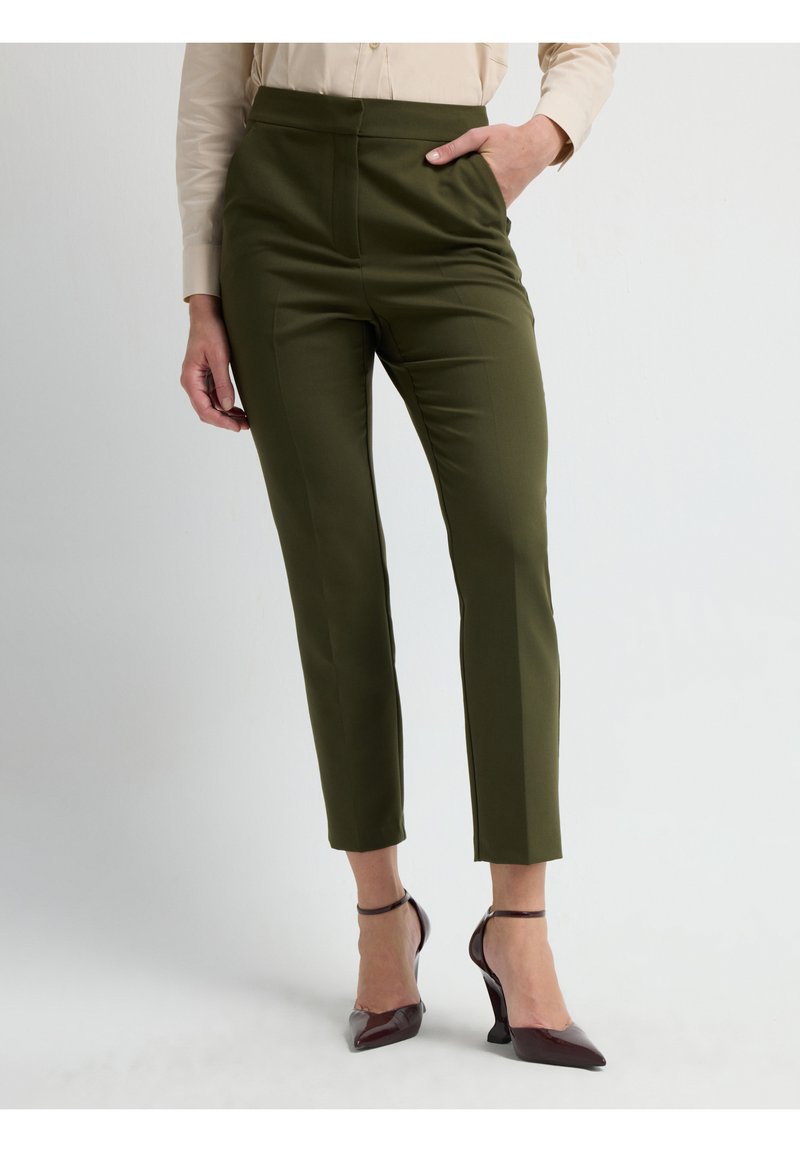Olijfgroene op maat gemaakte broek met een hoge taille en zijzakken, gecombineerd met bordeauxrode puntige hakken. Glad materiaal en slank ontwerp.