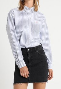 Randig skjorta i ljusblått och vitt, kombinerad med en svart jeanskjol med fransar och framfickor.