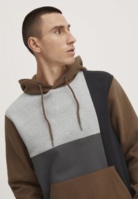 Hoodie met een patchworkontwerp in grijs, bruin, donkergrijs en zwart. Gemaakt van zachte stof met een verstelbaar trekkoord en een voorzak.