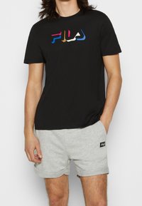Černé bavlněné tričko s barevným logem FILA v modré, oranžové, růžové a bílé barvě. V kombinaci se šedými šortkami, ukazujícími casual styl.