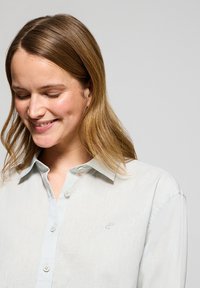 Ljusblå skjorta med knappar i lättviktsmaterial med en subtil struktur. Har en klassisk krage och en liten broderad logotyp på bröstet.