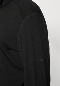 Camisa preta de mangas longas, feita de tecido texturizado, com um detalhe de costura ao longo do ombro e o logótipo "icebreaker" bordado na manga.