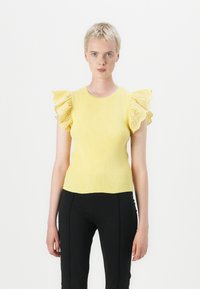 Gul ribbet gensarmer med korte flounce-ermer med øyelet detaljer. Sittende design, parret med svarte bukser; glatt tekstur.