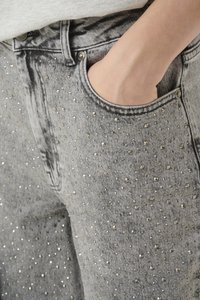 Pelēki denim džinsi ar pieguļošu dizainu, akcentēti ar metāla kniedēm, kas vienmērīgi izvietotas pa priekšu, un klasisku kabatu.