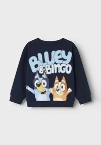 Marineblå hettegenser med et stort grafisk trykk av to tegneseriehunder, Bluey og Bingo, med fet tekst som sier "Bluey & Bingo." Myk blanding av bomull.