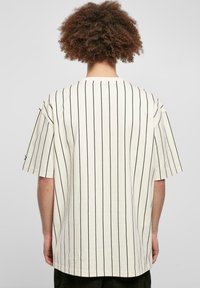 Overdimensioneret kortærmet t-shirt i off-white bomuld med sorte lodrette striber, rund hals og afslappet silhuet.