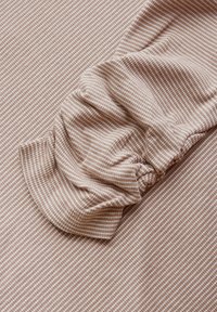 Tessuto a strisce marrone chiaro con dettagli nelle maniche arricciate, caratterizzato da una finitura testurizzata e sottili linee orizzontali. Materiale morbido ed elastico.