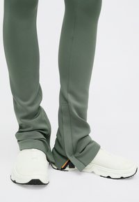 Πράσινα αθλητικά παντελόνια με λεία υφή, σε σχέδιο που στενεύει προς τα κάτω. Συνδυασμένα με λευκά φλατ παπούτσια με διχτυωτό επάνω μέρος και μαύρη σόλα.