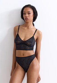 Schwarzer Spitzen-Bralette und dazu passende hochgeschnittene Bikinis, mit floralem Muster, durchsichtiger Textur, verstellbaren Trägern und figurbetontem Design.
