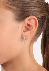 Orecchini d'argento con tre accenti a forma di stella, due piccole gemme blu e un ciondolo a forma di stella; progettati per pendere appena sotto il lobo dell'orecchio.