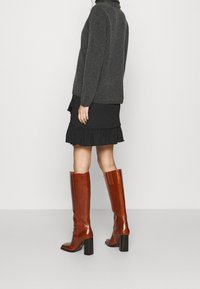 Bottes en cuir marron hautes jusqu'au genou avec un talon épais noir, présentant une surface lisse et un détail à nervures verticales à l'arrière.