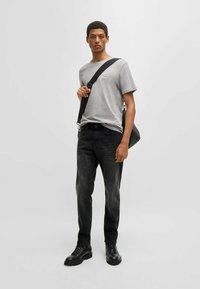 Camiseta gris de manga corta con un pequeño logo, combinada con jeans de mezclilla oscura y botas negras con cordones; sosteniendo un bolso negro de hombro.