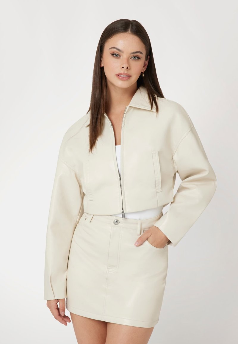 Trumpa kreminė dirbtinė odinė striukė su užtrauktuku, smailiu apykakle ir dviem priekinių kišenėmis, derinama su atitinkamu mini sijonu.