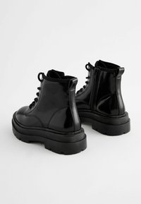 Bottes de cheville en cuir verni noir avec une semelle épaisse, un laçage à l'avant et une fermeture éclair sur le côté. Comprend une semelle en caoutchouc texturé noir et un design robuste.
