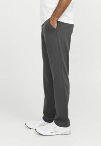 Pantalones de chándal grises hechos de una tela suave, con bolsillos laterales y un corte relajado. Combinados con zapatillas deportivas blancas para un look casual.