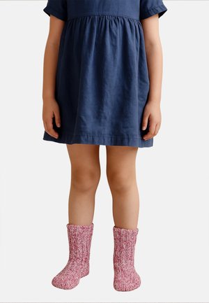Strick-Socken in enger Passform mit meliertem Muster in Rosa und Weiß, weicher Textur und geripptem Abschluss. Getragen zu einem dunkelblauen Baumwollkleid.