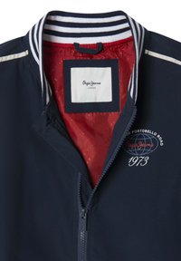 Marineblaue Zip-Up-Jacke mit gestreiftem Kragen, rotem Futter, gesticktem Logo und weißen Akzenten. Verfügt über einen glatten, leichten Stoff.
