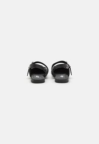 Sandalias negras con un acabado de cuero suave, suela plana, correas ajustables y un sutil detalle de hardware para mayor durabilidad y comodidad.
