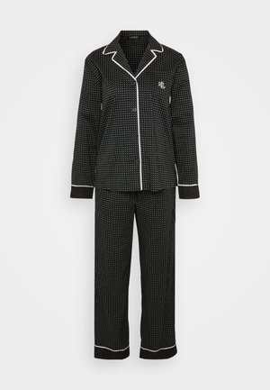 Svart pyjamassett med hvite prikker og hvit piping, som inneholder en knapp-oppskjorte og løse bukser, laget av myk tekstil for komfort.