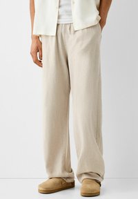 Beige linnen broek met een trekkoord in de taille en een wijd uitlopende design. Gestructureerde stof; gecombineerd met bruine instapschoenen.