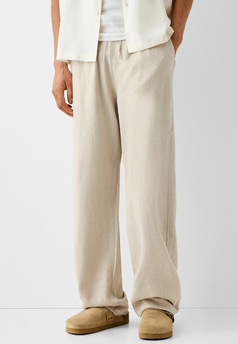 Beige linnen broek met een trekkoord in de taille en een wijd uitlopende design. Gestructureerde stof; gecombineerd met bruine instapschoenen.