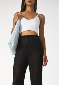 Biały krótki top na cienkich ramiączkach połączony z wysokim stanem, prześwitującymi czarnymi koronkowymi spodniami. Miękka niebieska torba trzymana pod pachą, minimalistyczny design.