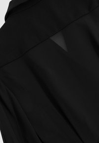 Fekete áttetsző blúz szilárd gallérral és hátsó résszel, könnyű, áramló anyagból és sima textúrával.
