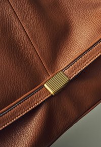 Sac en cuir brun avec une surface texturée, doté de quincaillerie dorée et d'un pli décoratif le long du bord supérieur.