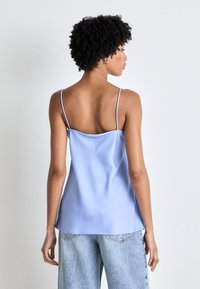 Cămașă de satin de culoare albastru deschis, cu bretele subțiri ajustabile, croială lejeră și textură netedă; asortată cu blugi largi de culoare albastru deschis, cu efect uzat.
