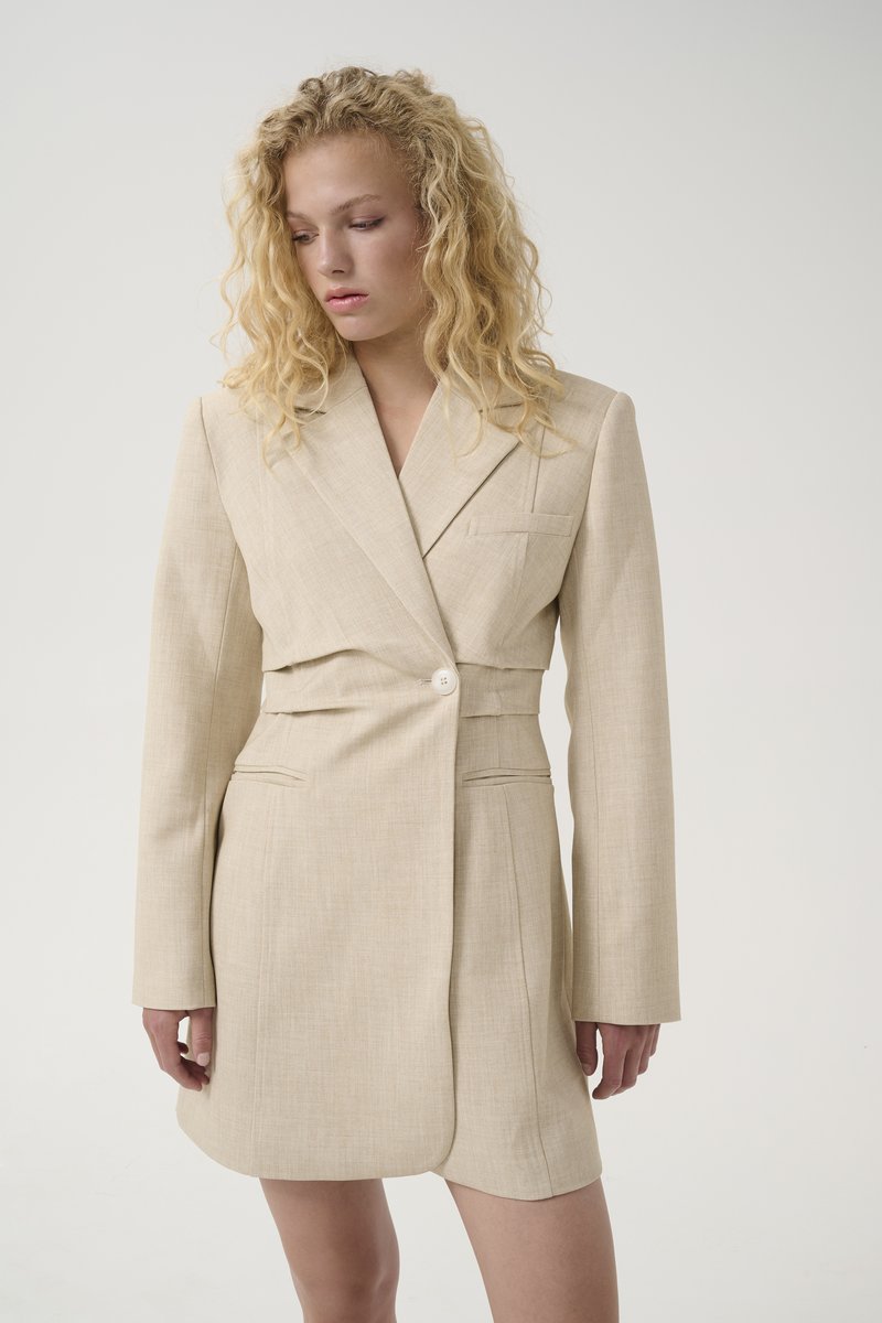 Robe blazer beige avec une taille cintrée, grands revers, manches longues, fermeture à un bouton et deux poches avant, fabriquée en tissu texturé.