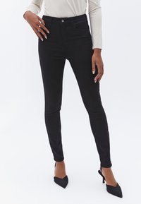 Jeans ajustados negros de mezcla de algodón, con una cintura alta, silueta ceñida y cierre de botón, con una textura suave.