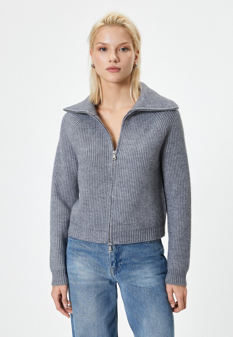 Grå ribbet zip-sweater med bred krave og tætsiddende kropsform. Har lange ærmer og en cropped længde, lavet af et blødt strikket materiale.