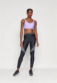 Lilla sports-BH og svarte leggings med grå detaljer. Leggingsene har et fargeblokkdesign og høyt liv. Treningsskoene er svarte.